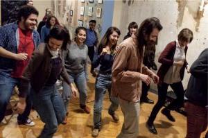 至少14个人的照片, 大多数人看起来都是20多岁,  穿着便服在木质地板的房间里跳舞.