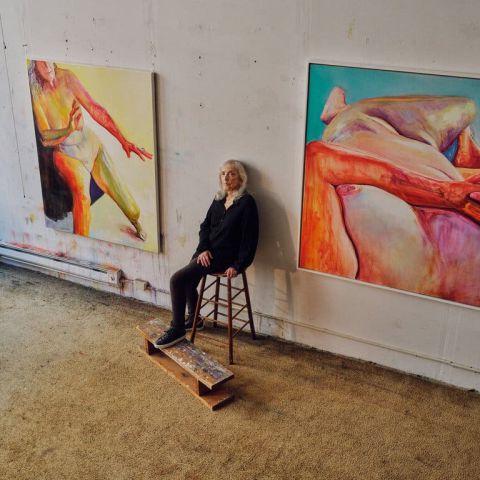 Joan Semmel sits in studio between two paintings